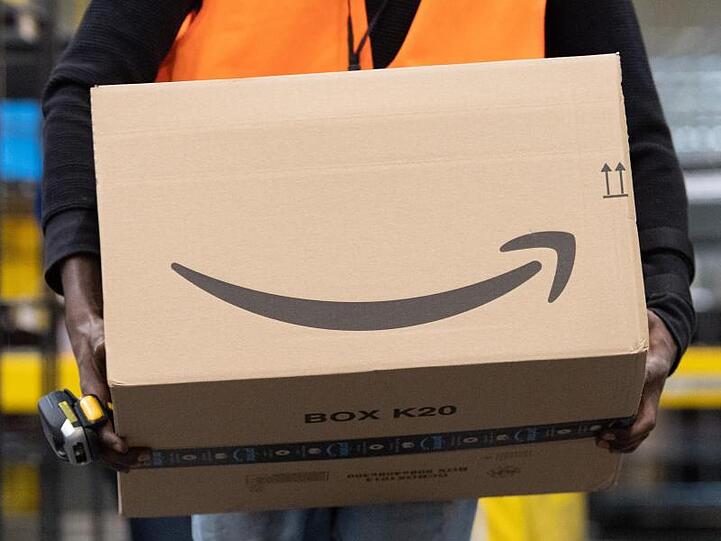Ein Sortiermitarbeiter von Amazon trägt in einem Verteilzentrum ein Paket. Verbraucherschützer sehen die zunehmende Marktmacht großer Online-Plattformen wie Amazon mit Sorge.