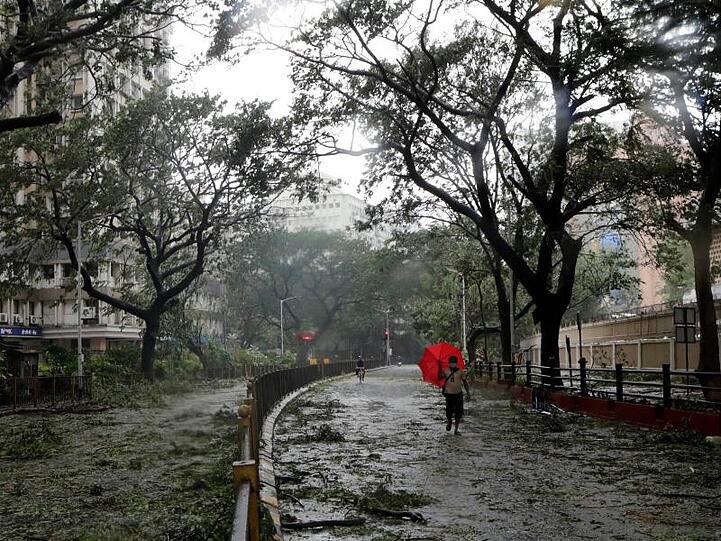 Ein Mann mit einem Regenschirm geht über eine Straße in Mumbai, auf der vom Wind abgerissene Äste und Blätter liegen.