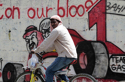 Ein Mann fährt auf dem Fahrrad an einem Graffiti vorbei, das Bilder von Bernie Ecclestone und dem König von Bahrain, Hamad bin Isa, zeigt.