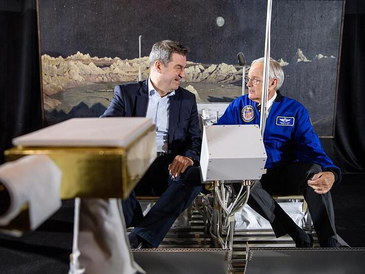 Söder (CSU, l.) und Duke sitzen in Mondauto-Nachbau vor Ölgemälde "Ideale Mondlandschaft" (1919) von Wilhelm Kranz. Foto: Matthias Balk