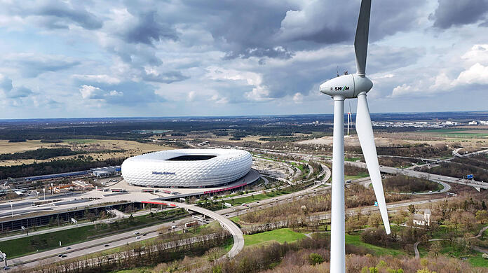Eines der beiden Windräder der Stadtwerke München, im Hintergrund die Allianz Arena.