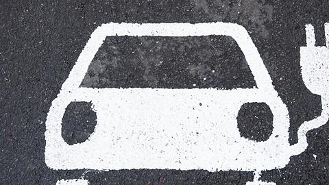 Ein Symbol für ein E-Auto markiert einen Parkplatz neben einer E-Ladesäule.