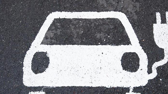 Ein Symbol für ein E-Auto markiert einen Parkplatz neben einer E-Ladesäule.