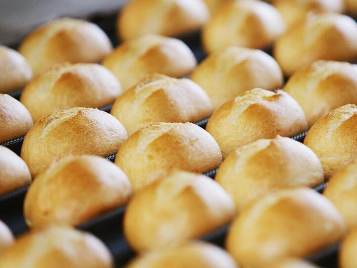 Brötchen auf dem Fließband in einer Großbäckerei kommen aus dem Ofen. Foto: Achim Scheidemann/dpa/Archivbild