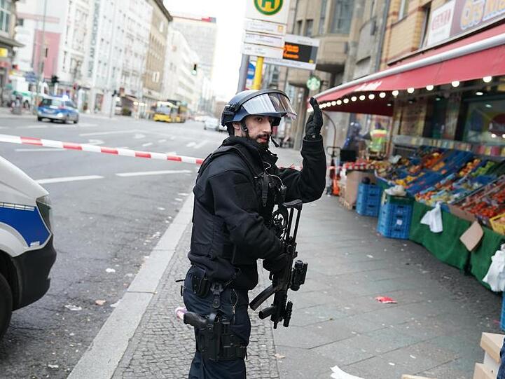 Ein Polizist in Schutzausrüstung weist Passanten an, sich in Sicherheit zu bringen.