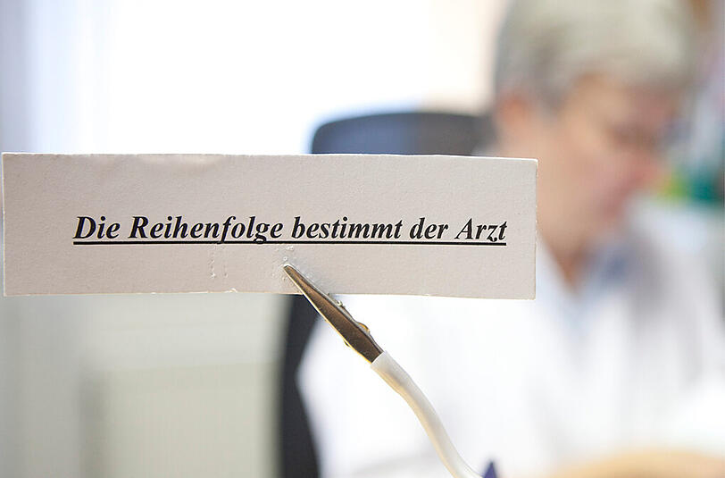 Ein Schild weist in einer Arztpraxis darauf hin, dass die Reihenfolge der Patienten vom Arzt bestimmt wird. Eine Servicestelle für Facharzt-Termine startet nun auch in Bayern.