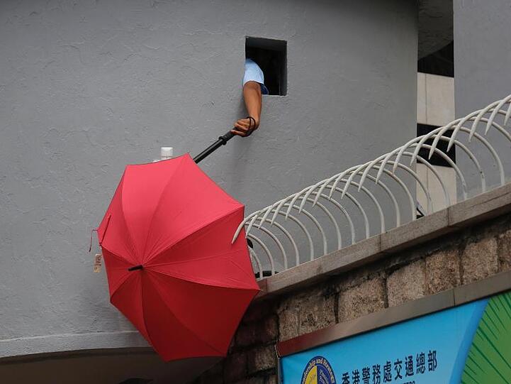 Ein Polizist versucht, einen Regenschirm zu entfernen, der den Blick der Überwachungskameras vor dem Polizeipräsidium in Hongkong blockiert.
