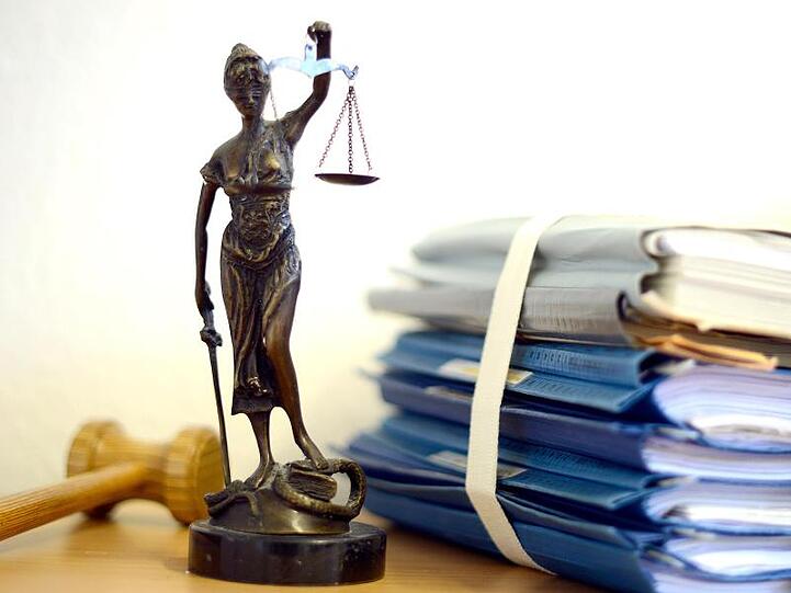 Die modellhafte Nachbildung der Justitia steht neben einem Holzhammer und einem Aktenstapel. Foto: Volker Hartmann/dpa