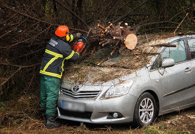 Ein Feuerwehrmann zersägt in Hamburg-Rahlstedt einen auf ein Auto gestürzten Baum.