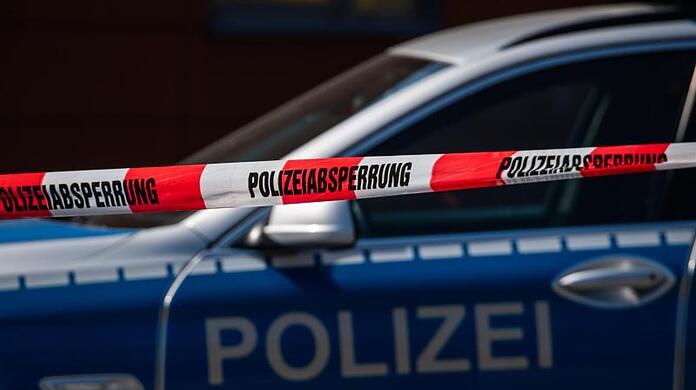 Ein Polizeiauto steht hinter einem Absperrband der Polizei.