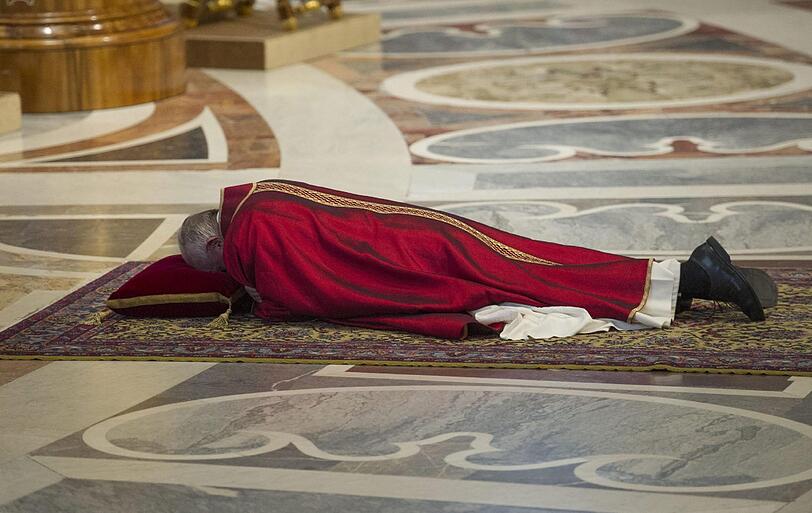 Papst Franziskus betet auf dem Boden liegend.