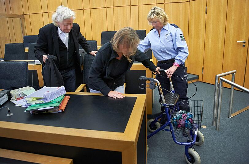 Die Angeklagte, Katja R., gestützt von einem Rollator und einer Justizmitarbeiterin in Begleitung ihres Anwaltes Siegmund Benecken (l) im Saal des Landgerichts in Münster. (Archivbild)