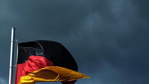 Eine Deutschlandfahne vor dunklen Wolken.