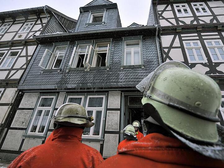 Einsatzkräfte der Feuerwehr blicken auf das ausgebrannte Haus.