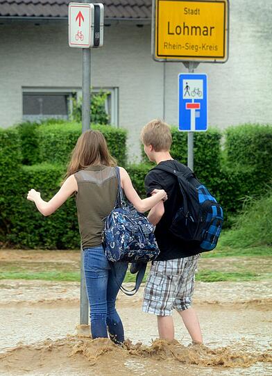 Kinder laufen am 20.06.2013 über eine überschwemmte Straße in Lohmar.