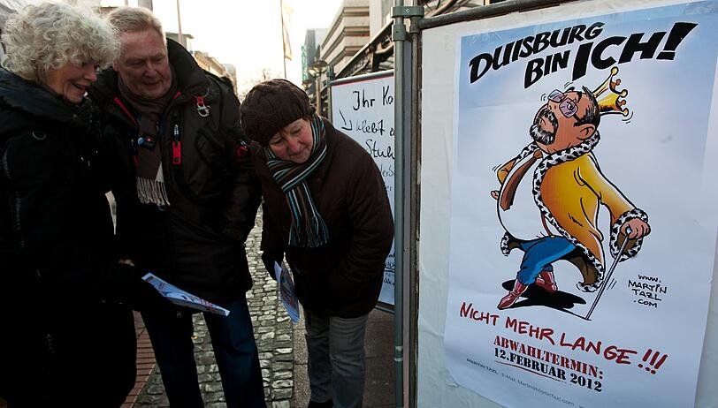 Passanten betrachten am Donnerstag in Duisburg eine Karikatur des Kuenstlers Martin Tazl vom Oberbuergermeister von Duisburg, Adolf Sauerland (CDU), mit der Ueberschrift "Duisburg bin ich!" und der Unterschrift "Nicht mehr lange!!!"