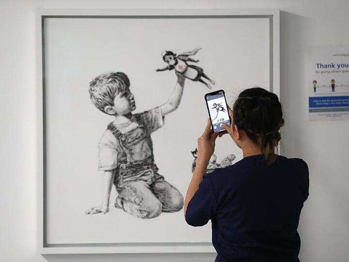 Eine medizinische Mitarbeiterin fotografiert das Banksy-Kunstwerk mit dem Titel "Game Changer".