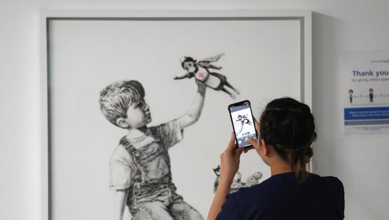 Eine medizinische Mitarbeiterin fotografiert das Banksy-Kunstwerk mit dem Titel "Game Changer". Eine medizinische Mitarbeiterin fotografiert das Banksy-Kunstwerk mit dem Titel "Game Changer".