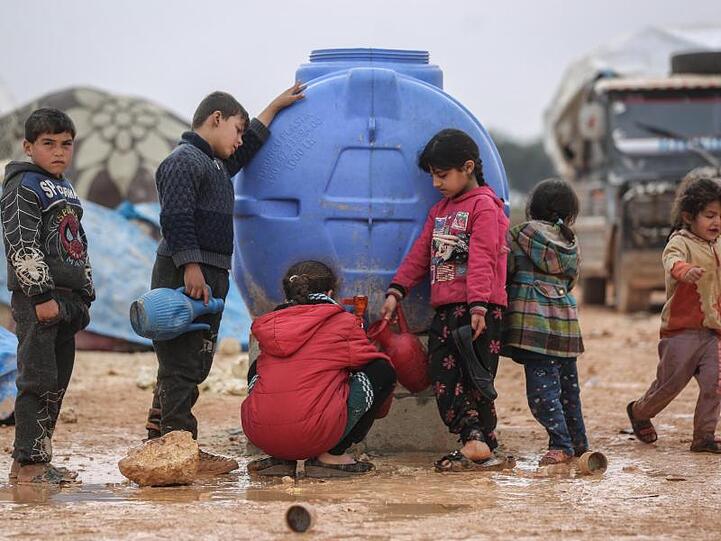 Kinder füllen Kannen in einer Notunterkunft für Familien mit Wasser.