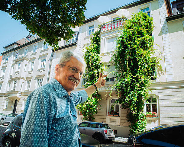 Ude zeigt auf sein Wohnhaus. An der Fassade klettern die selbst gepflanzten Kiwis empor.