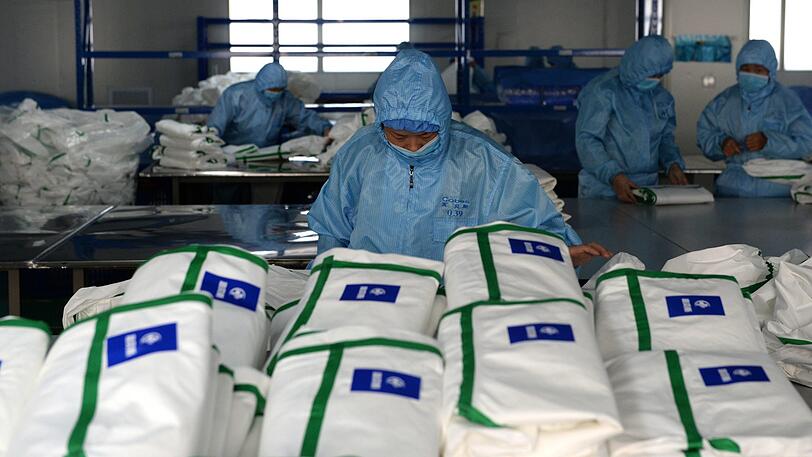 Mitarbeiter eines medizinischen Unternehmens stehen in einer Fertigung für Schutzanzüge. Die Zahl der Infektionen und Todesopfer durch die Lungenkrankheit aus China ist erneut gestiegen.