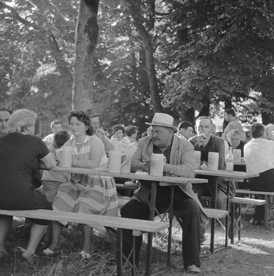 Eigentlich ist's doch ein schöner Tag, die Frauen haben sich die Perlenkette herausgesucht und das Sommerkleid gebügelt, aber für den grantigen Herrn mit Hut scheint dieser Tag im Sommer 1953 kein glücklicher zu sein. Zumindest scheint er keine gute Zeit zu haben, trotz Sonne, trotz Bier im Steinkrug, trotz Zeit im Ausflugslokal in Grasbrunn. Der auf dem Tisch zu sehende Krug, der Keferloher, stammt übrigens genau von hier - daher auch der Name. Das Bier fließt hier schon seit Jahrhunderten, nach der Schlacht auf dem Lerchenfeld, bei der Otto der Große 955 seinen größten militärischen Sieg feierte und die Ungarn zurückdrängte, wurde Keferloh ein Umschlagplatz für die Pferde der besiegten ungarischen Soldaten. Daraus entwickelte sich ein Viehmarkt und schließlich auch ein Bier- und Landwirtschaftsfest.