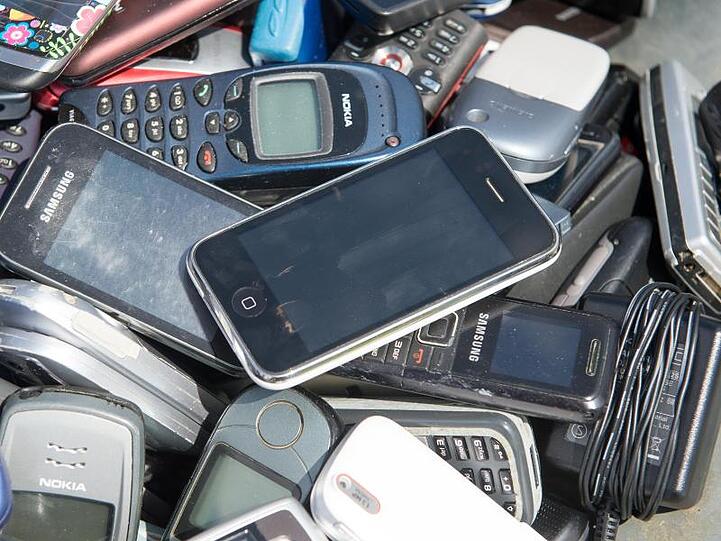 Alte Mobiltelefone liegen in einer Schubkarre.