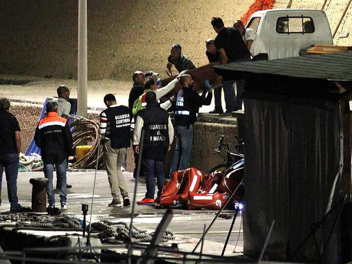 Mitarbeiter der italienischen Küstenwache bringen im Hafen von Lampedusa einen Sarg von Bord.