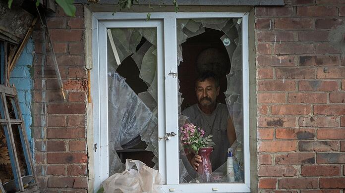 Ein Mann in Bachmut stellt in seinem durch russischen Beschuss beschädigten Haus Blumen  auf die Fensterbank.