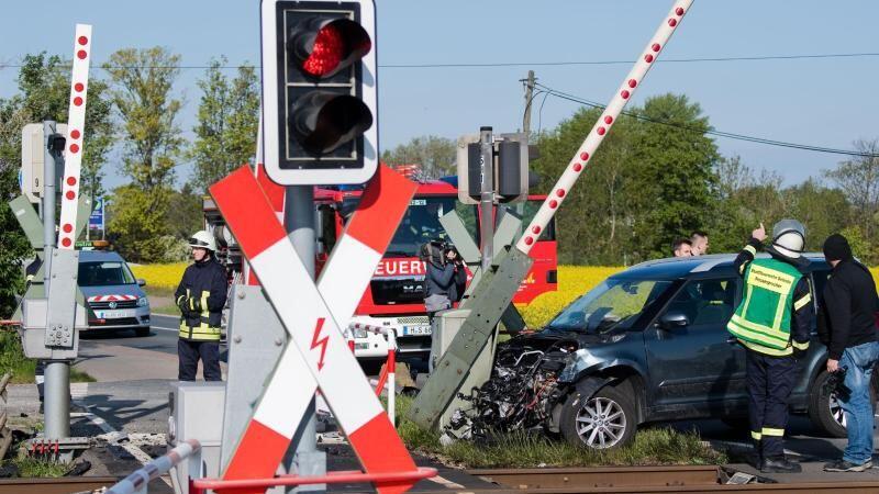 Ein beschädigter Pkw klemmt unter einer Bahnschranke. Feuerwehrleute sichern die Unfallstelle.