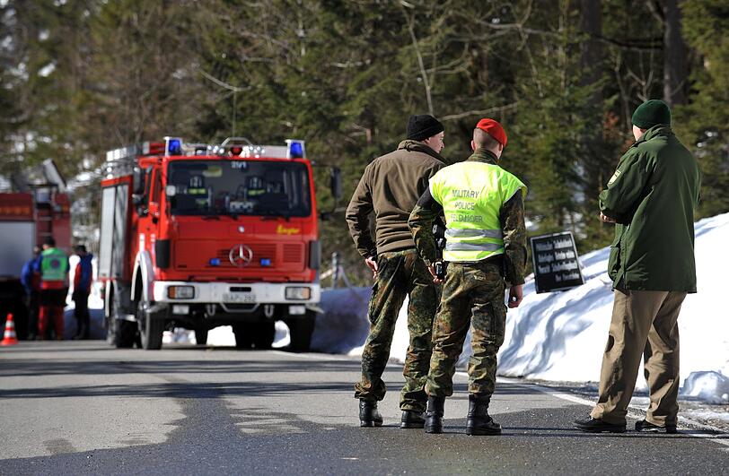 Feldjäger der Bundeswehr und ein Polizist stehen vor den Einsatzfahrzeugen der Feuerwehr.