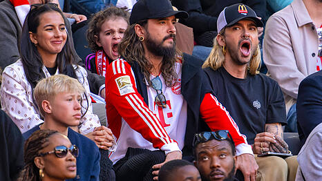 Tom und Bill Kaulitz bei einem Fußballspiel des FC Bayern. Während Tom gebannt das Spielgeschehen verfolgt, wirkt Bill gelangweilt.