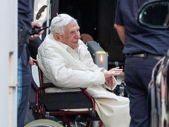 Der emeritierte Papst Benedikt XVI wird in Regensburg mit einem Rollstuhl in einen Bus geschoben. Foto: Daniel Karmann/dpa/Archivbild
