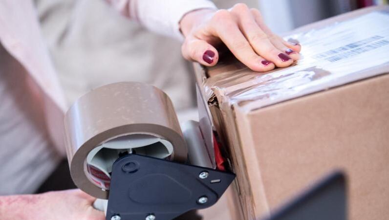 Eine Frau verpackt ein Paket. Muss sie für die Rücksendung bald bezahlen? Eine Frau verpackt ein Paket. Muss sie für die Rücksendung bald bezahlen?