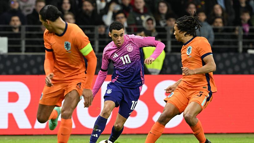 Deutschlands Jamal Musiala (M) kämpft gegen Nathan Aké aus den Niederlanden () und Virgil van Dijk um den Ball.