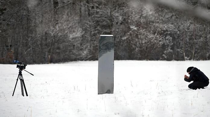 Unterhalb des Schlosses Neuschwanstein auf einer Wiese im Schnee steht der Monolith aus Metall.