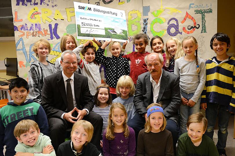 Martin Janke, Geschäftsführer der SWM Bildungsstiftung (links), und Gerd Grüneisl von
Kultur und Spielraum e.V. bei der Scheckübergabe vor der &bdquo;Sprachtapete&ldquo; in der Grundschule
an der Farinellistraße.