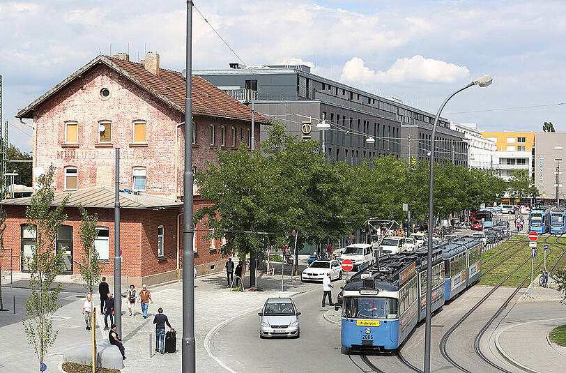 Moosacher Kontrast: das alte Bahnhäuschen aus Backstein neben einem großen, modernen und tiefgrauen Hotelkomplex.