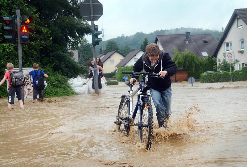 in Junge schiebt am 20.06.2013 sein Fahrrad über eine überschwemmte Straße in Lohmar (Nordrhein-Westfalen). Heftige Gewitter haben in Nordrhein-Westfalen zu zahlreichen Rettungseinsätzen der Feuerwehr geführt.