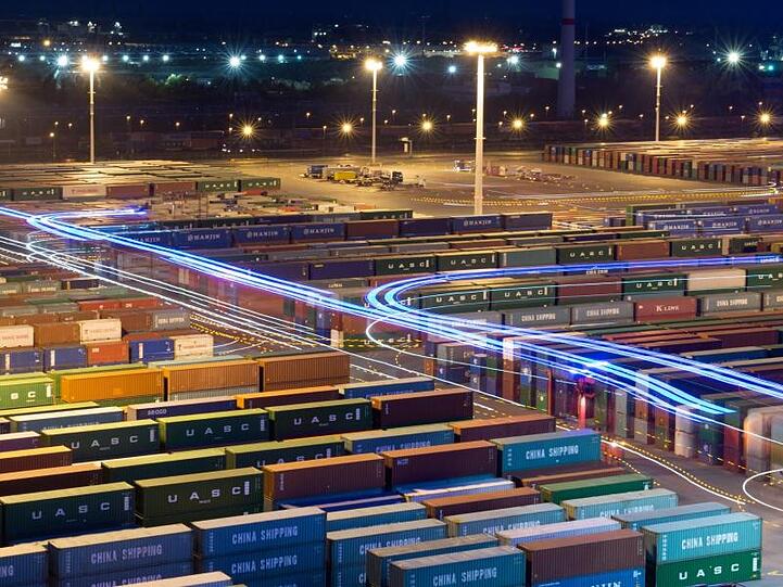 Hubwagen zum Umschlag von Containern fahren mit blauer Beleuchtung im Hamburger Hafen zwischen abgestellten Containern.