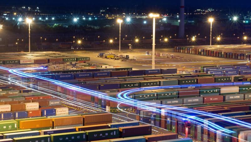 Hubwagen zum Umschlag von Containern fahren mit blauer Beleuchtung im Hamburger Hafen zwischen abgestellten Containern. Hubwagen zum Umschlag von Containern fahren mit blauer Beleuchtung im Hamburger Hafen zwischen abgestellten Containern.