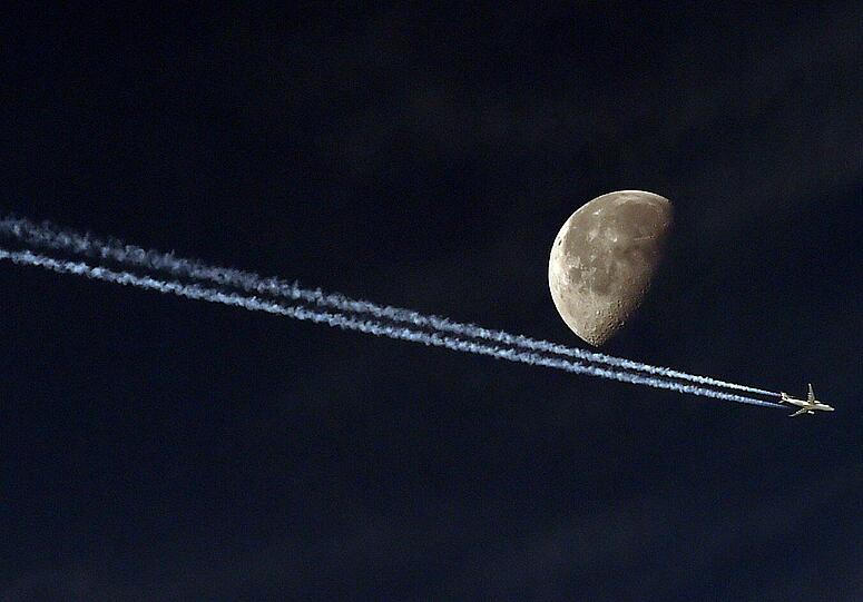 Ein Flugzeug hinterlässt einen Kondensstreifen, während es aus Sicht des Fotografen den Mond passiert. Das Bild wurde in der algerischen Hauptstadt Algier aufgenommen.