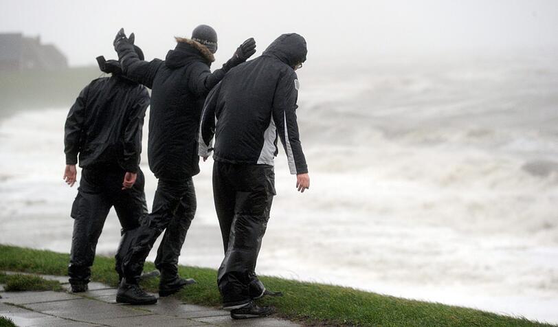Drei Männer stemmen sich in Dagebüll (Schleswig-Holstein) gegen den Sturm