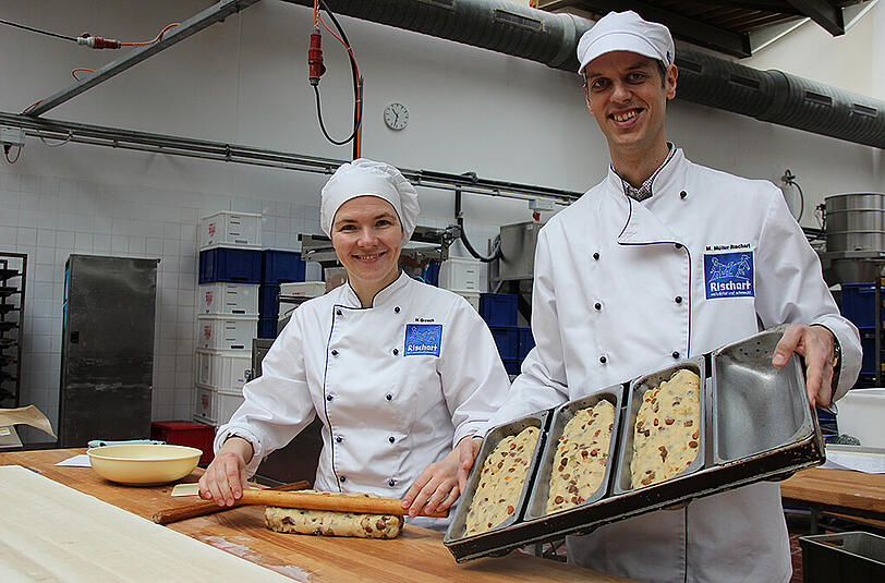 Produktionsleiterin Heike Grosch zeigt, wie der Stollen mit einem französischen Rollholz seine typische Hauben-Form erhält. Magnus Müller-Rischart hat schon die Backform parat.