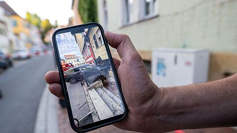 Der Hausbesitzer zeigt auf seinem Handy das Bild von dem Auto, das in der Hauswand steckt.