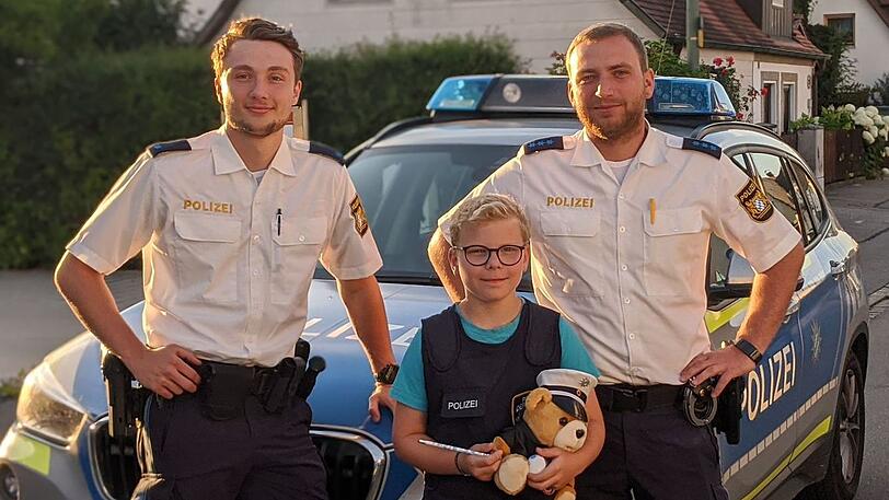 Der neunjährige Elias steht zwischen zwei Polizeibeamten. Er war zur Stelle, als die Beamten in einem Gebüsch vor dem Garten der Familie mit Taschenlampen nach Drogen suchten.