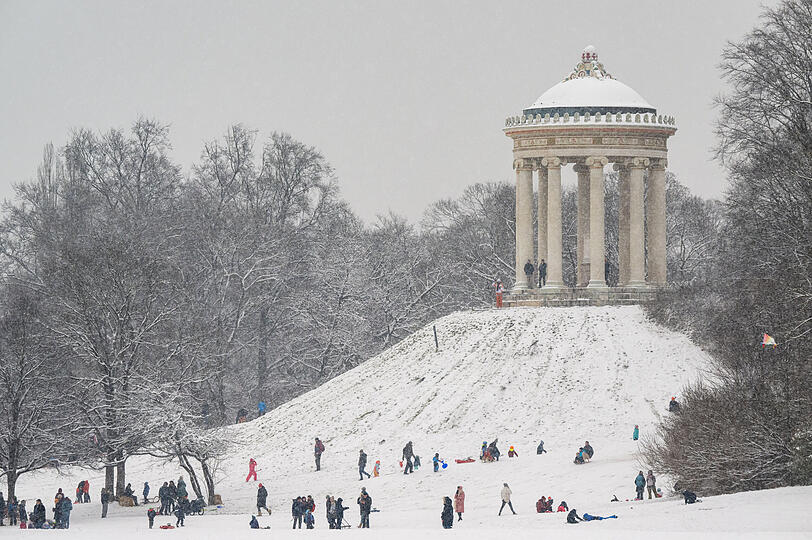Kinder und Erwachsene rodeln am Hügel des Monopteros im Englischen Garten. Der Schnee hat die weitläufige Parkanlage in eine Winterlandschaft verwandelt.