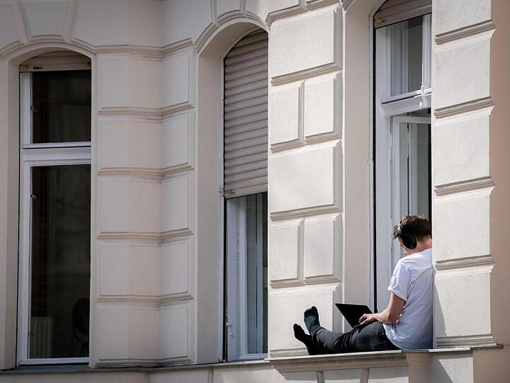 Ein Mann hat sein Homeoffice auf die sonnige Fensterbank seiner Wohnung verlegt. Foto: Kay Nietfeld/dpa/Archivbild