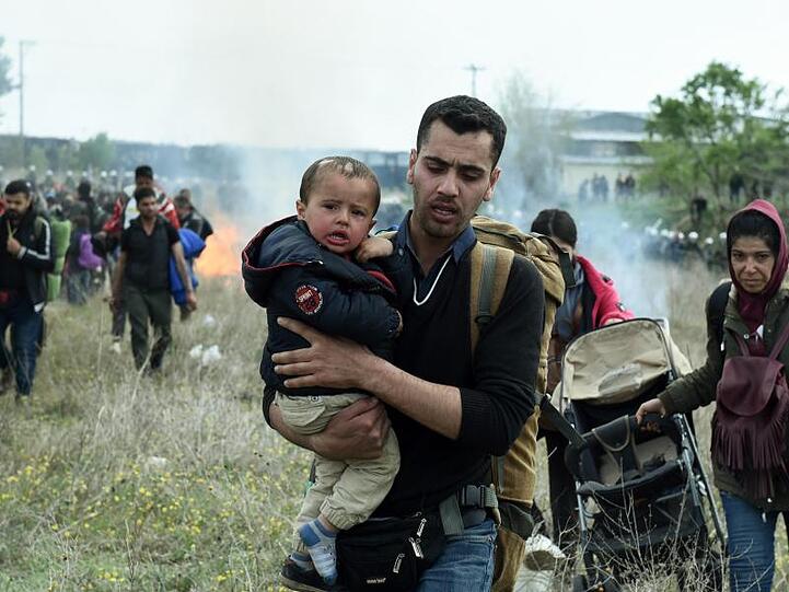 Ein Mann hält ein Baby auf dem Arm, während die Bereitschaftspolizei Tränengas einsetzt.