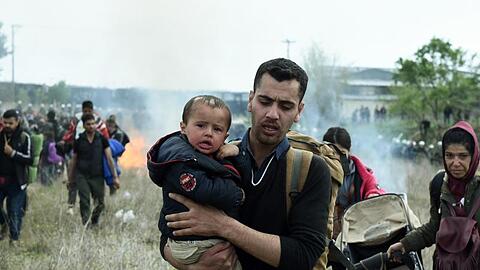 Ein Mann hält ein Baby auf dem Arm, während die Bereitschaftspolizei Tränengas einsetzt.
